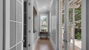 A hallway with a wooden floor, white walls, and large glass doors leading to an outdoor area with plants.
