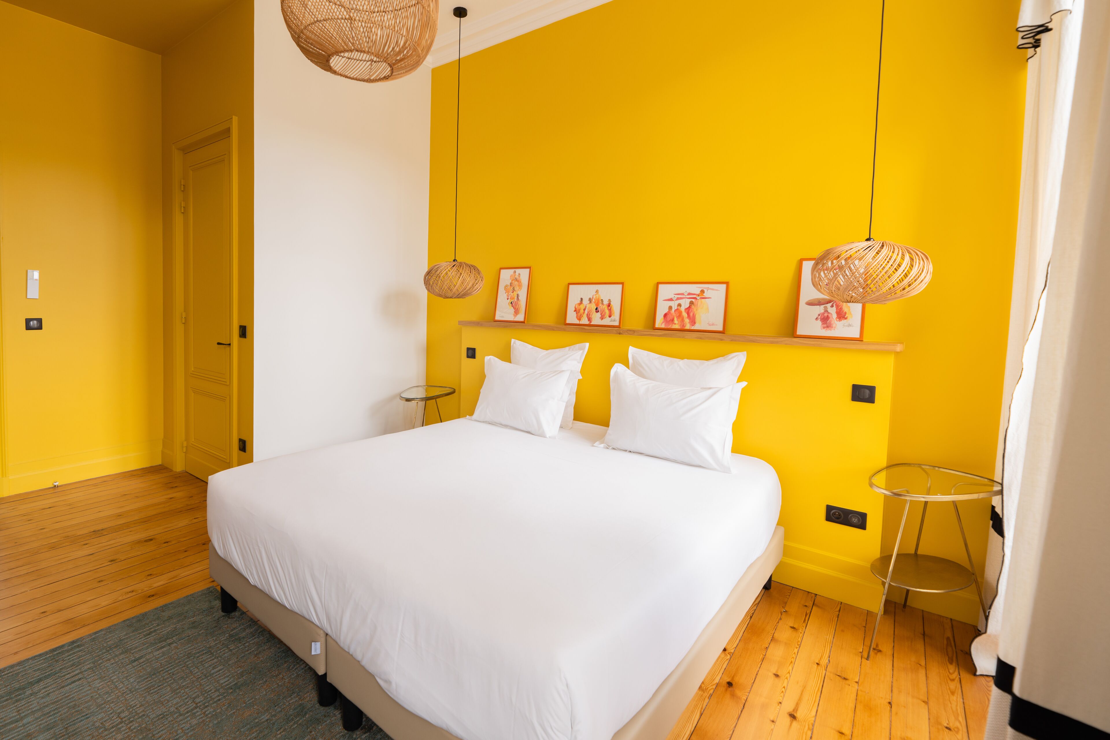 A room with a bed, wooden floor, yellow walls, and a white ceiling.