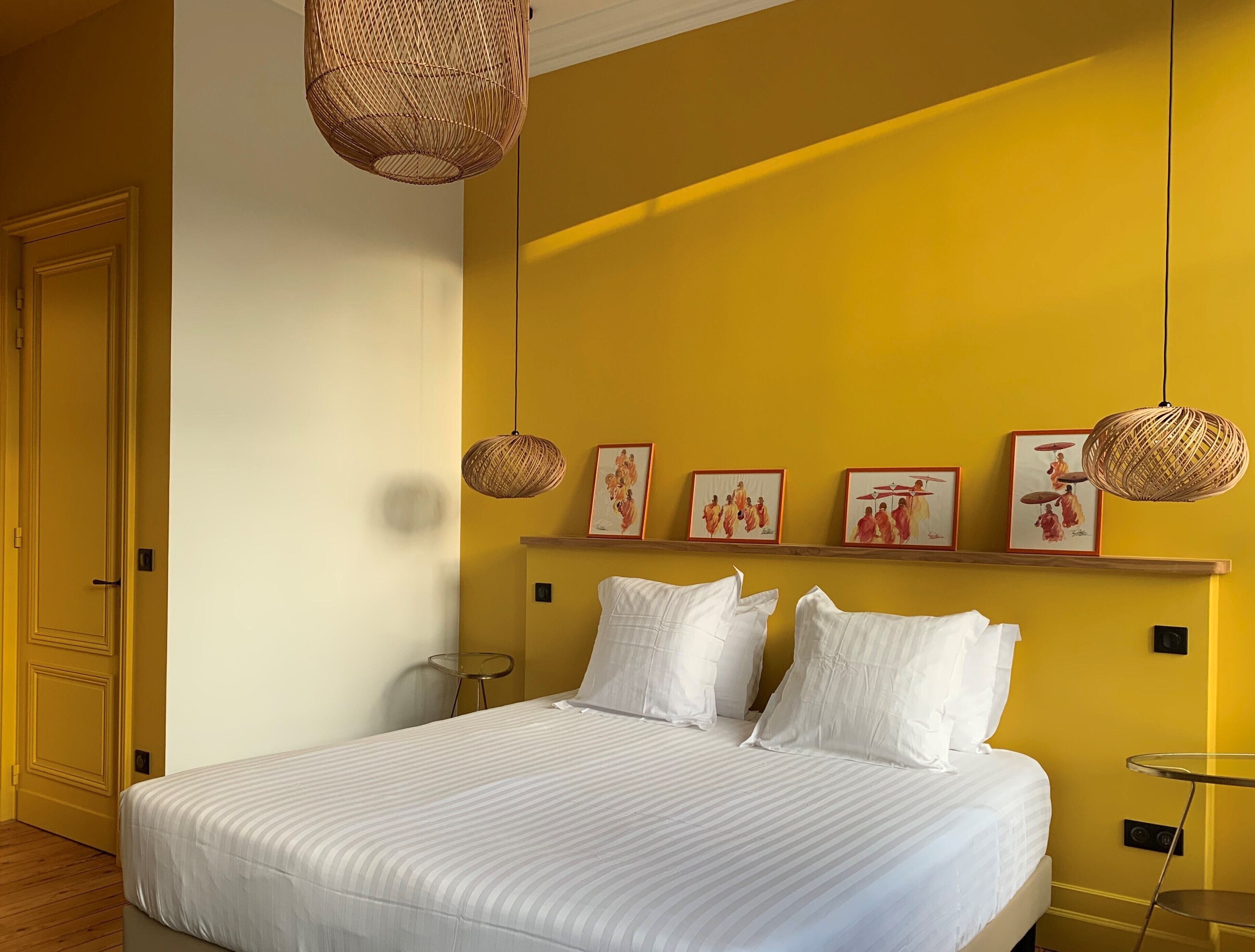 A bedroom with a bed, white bedding, a yellow wall, and framed artwork.