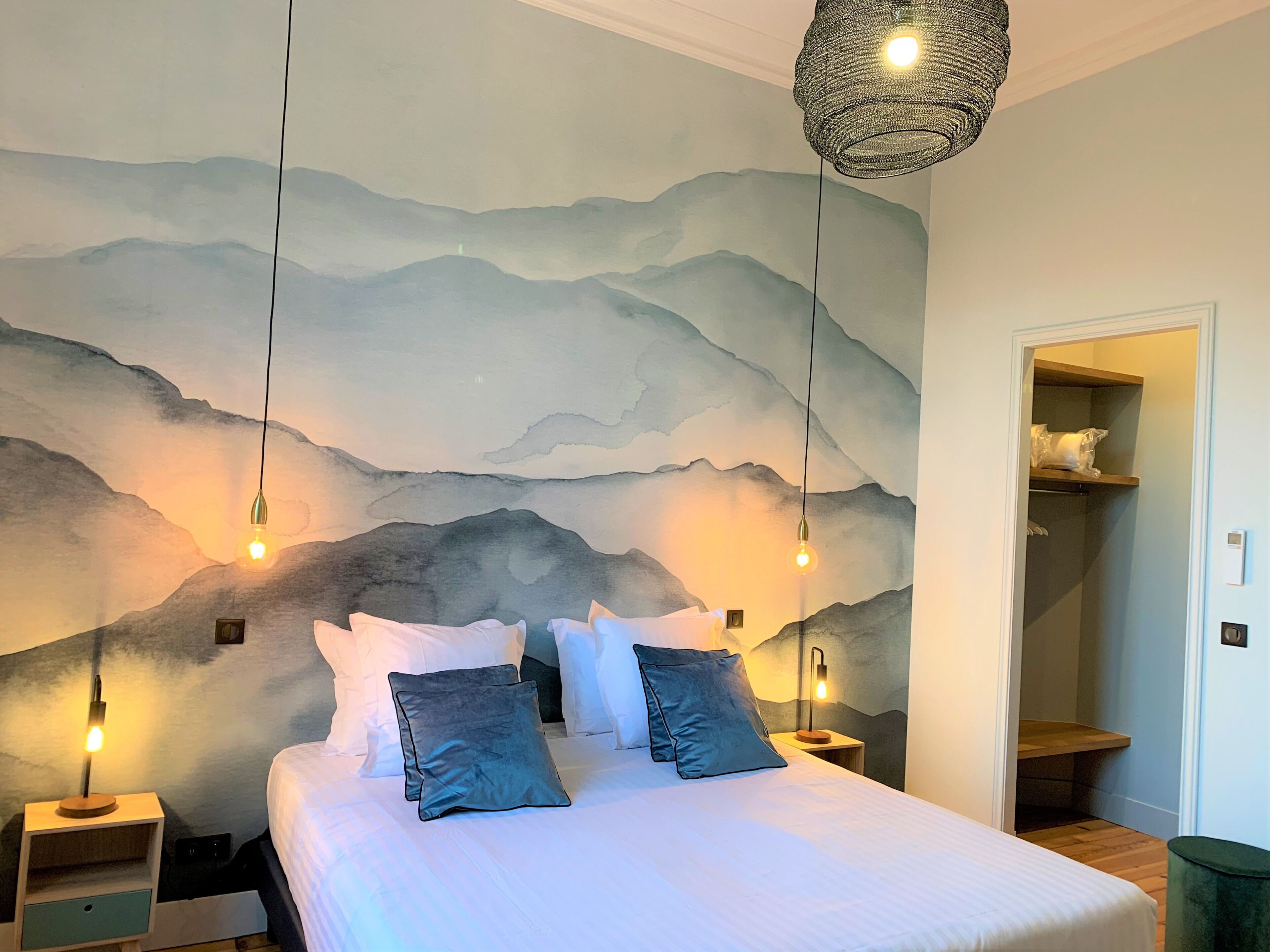 A bedroom with a large bed, two bedside tables, a wall-mounted lamp, and a door leading to a closet.