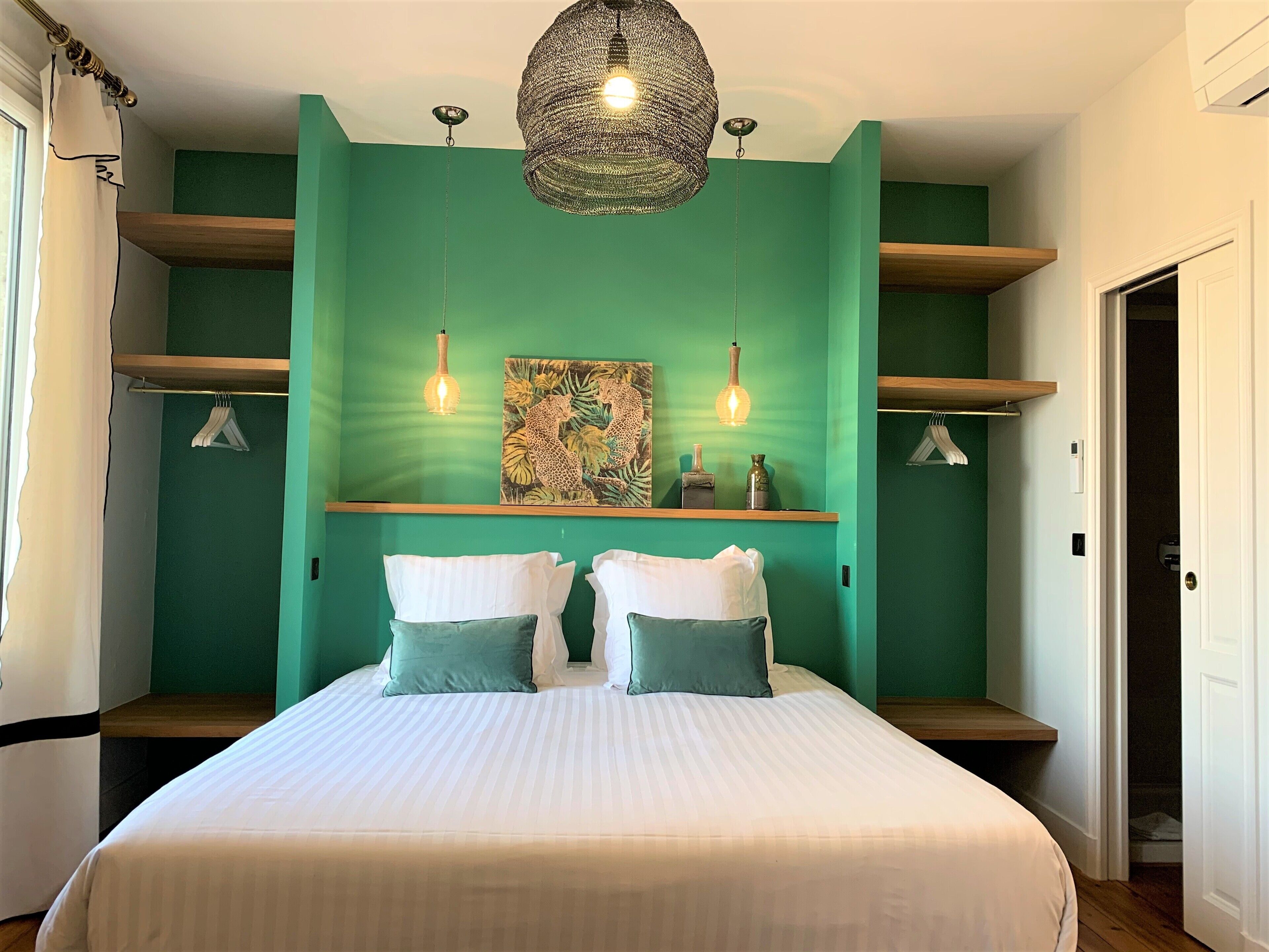 Un dormitorio con cama, dos almohadas, una lámpara colgante, una repisa con objetos decorativos y una puerta.