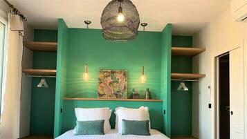 Un dormitorio con cama, dos almohadas, una lámpara colgante, una repisa con objetos decorativos y una puerta.