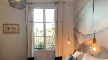 Une chambre avec un grand lit, du linge de lit blanc, une vue par la fenêtre et un luminaire fixé au mur.