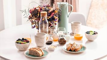 A breakfast table with various food items, a pitcher, and a vase of flowers.