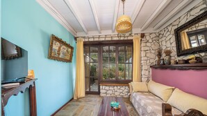 Una habitación con pared de piedra, un banco de madera, un sofá, una mesa de madera y un televisor sobre un mueble.