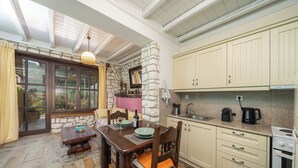Una cocina con pared de piedra, armarios de madera, una mesa de comedor con sillas y vistas a través de un ventanal.