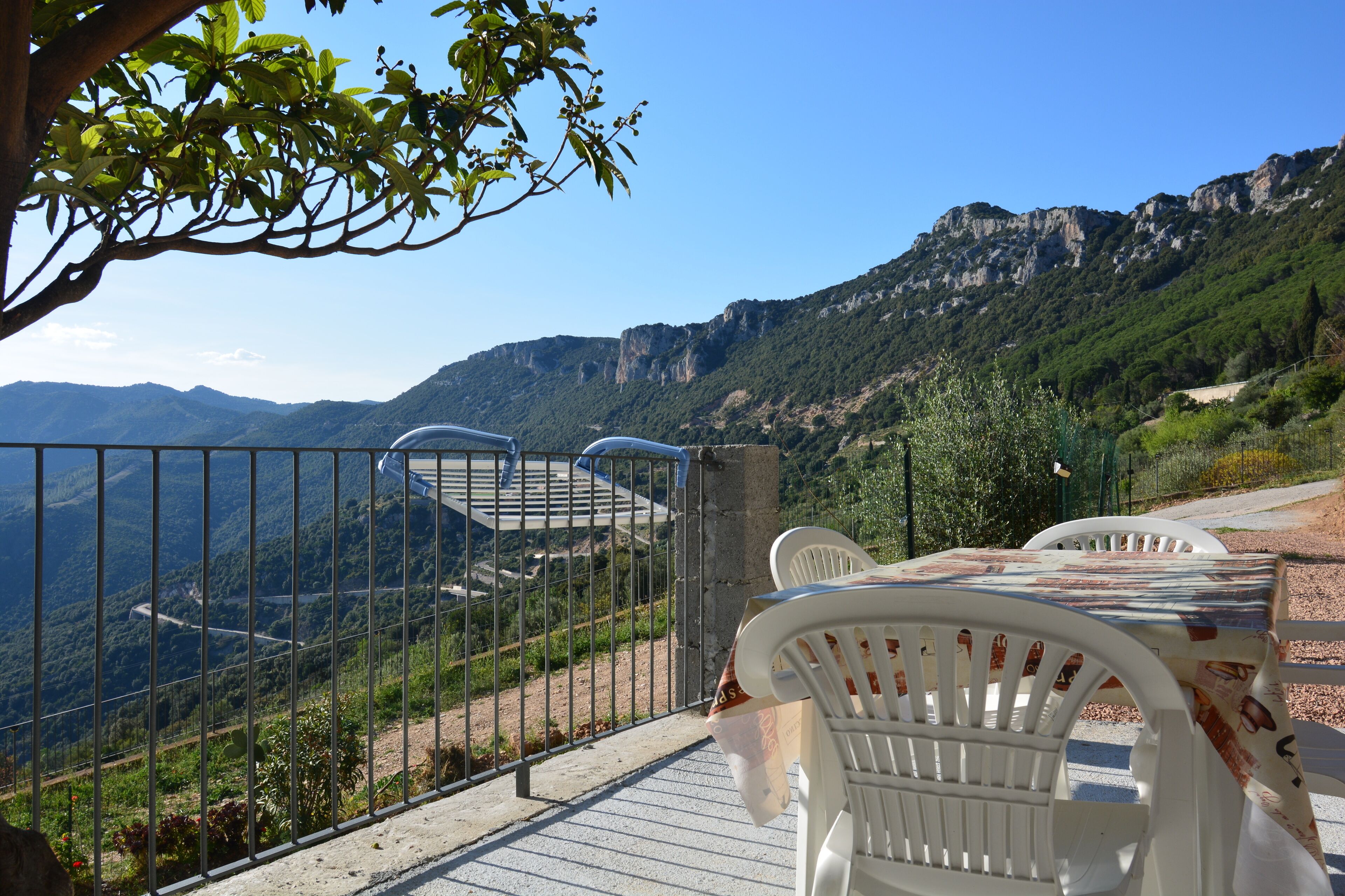 A terrace with white plastic chairs and a table, overlooking a mountainous landscape.