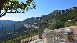 A terrace with white plastic chairs and a table, overlooking a mountainous landscape.