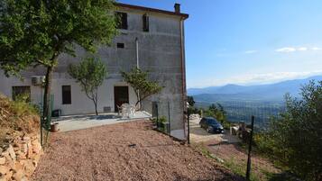 A two-story building with a gravel driveway, a fenced area, and a view of distant mountains.