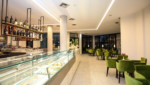 A modern bar area with a glass display case and shelves of bottles. There are green chairs arranged for seating. - Hotel Regina Garden Vlore (Vlorë)