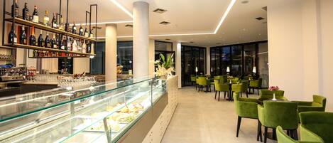 A modern bar area with a glass display case and shelves of bottles. There are green chairs arranged for seating.