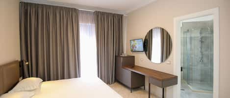 A hotel room with a bed, a desk, a TV, and a shower area.