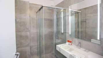 A modern bathroom with a glass-enclosed shower, a marble sink, and a large mirror.