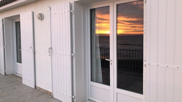 Un bâtiment aux murs extérieurs blancs et doté d’un balcon donnant sur la mer, au moment du coucher du soleil.