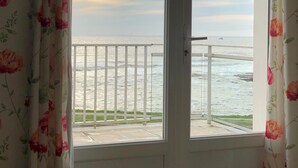 Une chambre avec vue sur la mer, accessible par une porte-fenêtre donnant sur un balcon.