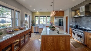 A modern kitchen with wooden cabinets, stainless steel appliances, and a large island with a bowl of fruit.