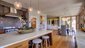 A modern kitchen with a large island, pendant lights, and a dining area with bar stools.