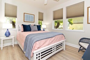 A bedroom with a bed, two bedside tables, a chair, and windows with blinds.