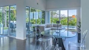 Una sala de estar moderna con una mesa y sillas de vidrio, un sofá y grandes puertas correderas de vidrio que dan a un balcón con mobiliario exterior.