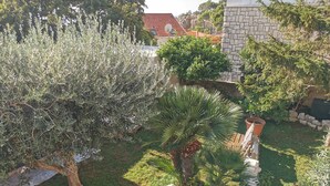 Un jardín con diversas plantas, un muro de piedra y un edificio con techo rojo al fondo.