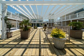 A covered outdoor deck with a wooden floor, potted plants, and a white railing. - Colorful Atrium Villa! Great Location! Across from Beach! Pet Friendly!! Amenity access included! (Seabrook Island)
