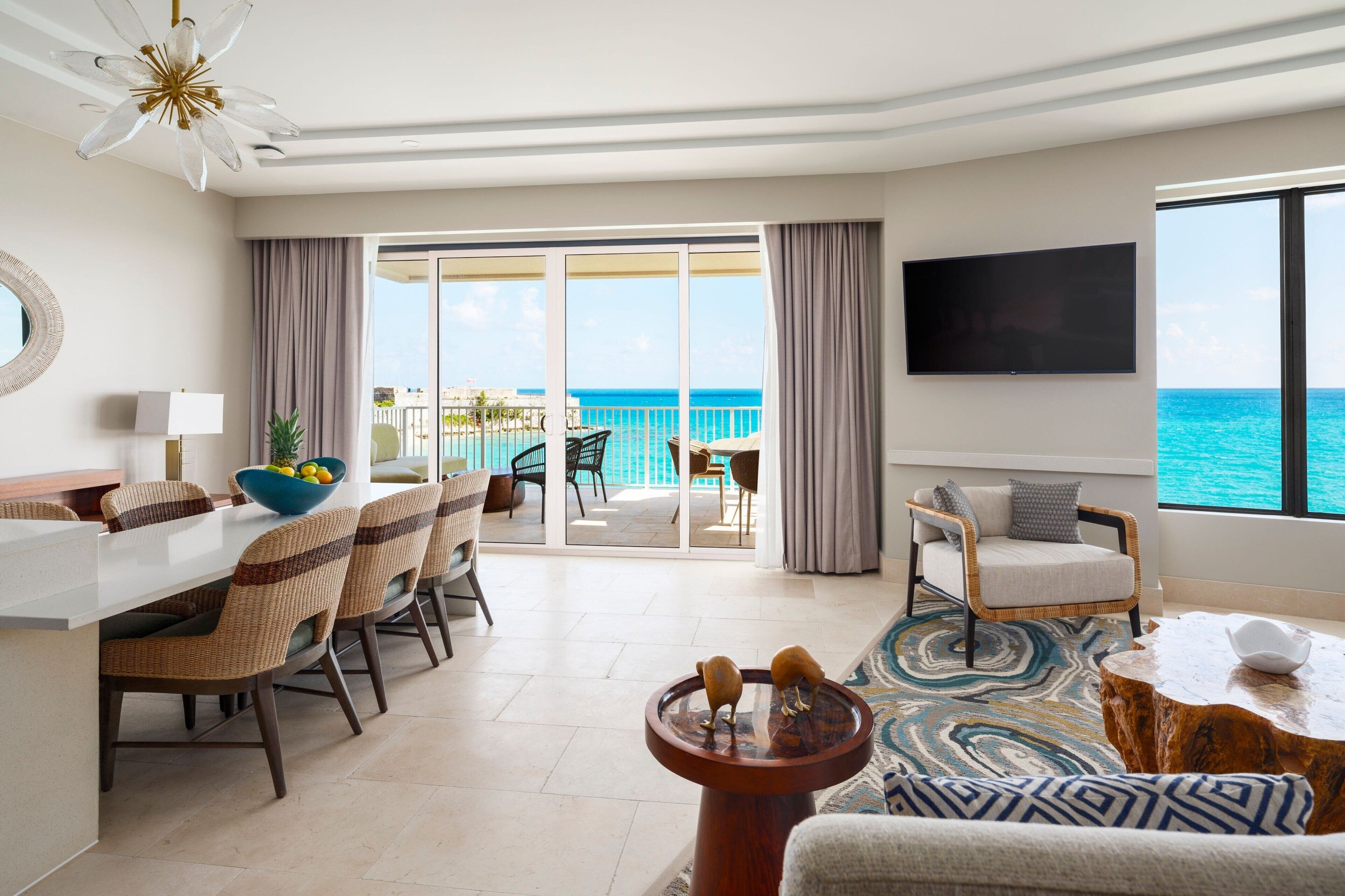 Quarto de hotel moderno com área de refeições, espaço de estar com vista para o oceano e televisão de tela plana na parede.