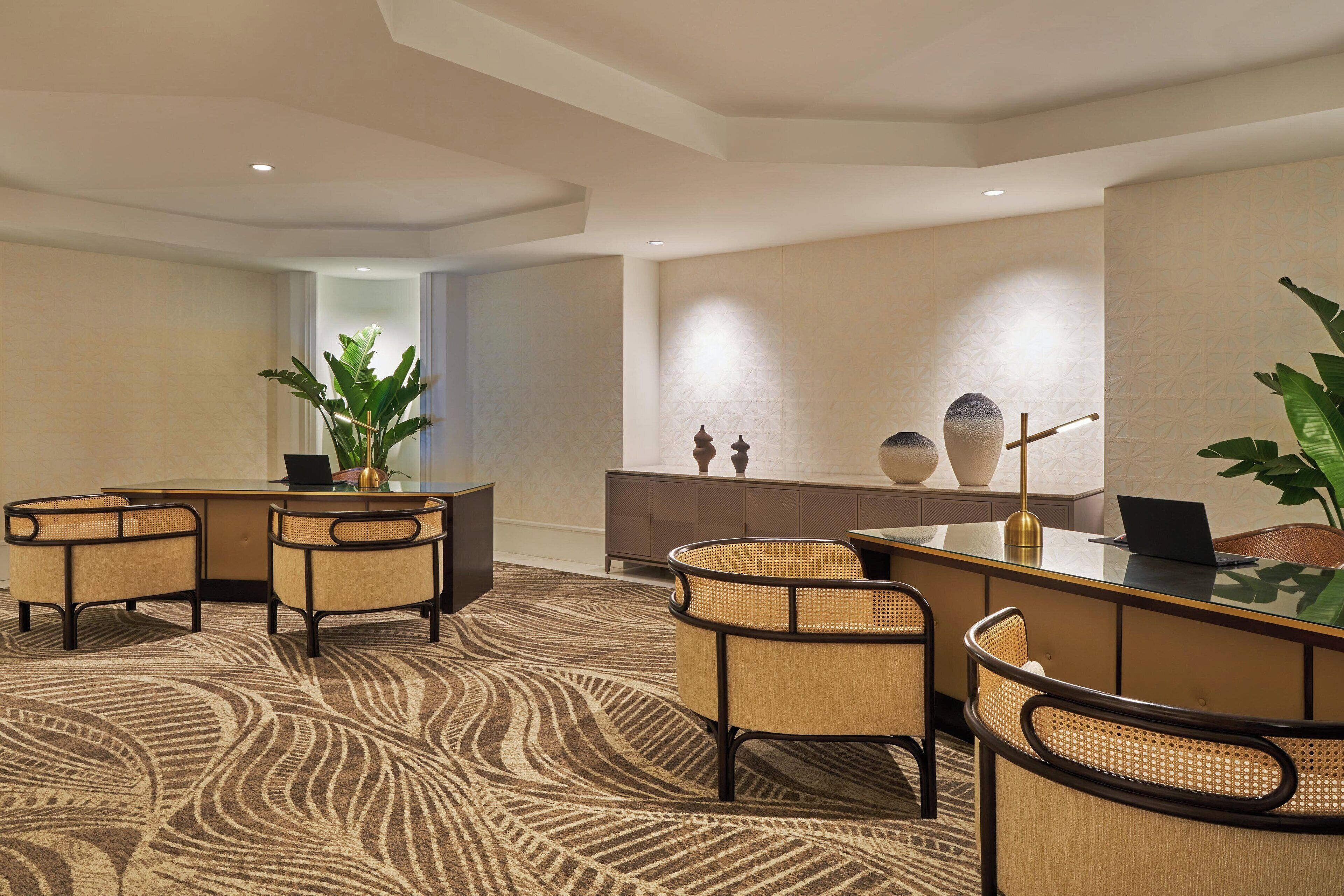 A reception area with a curved reception desk, two wicker chairs, a large potted plant, and a decorative vase on the wall.
