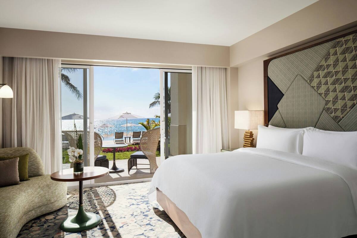 A hotel room with a large bed, a small table, a chair, and a view of the outdoors.