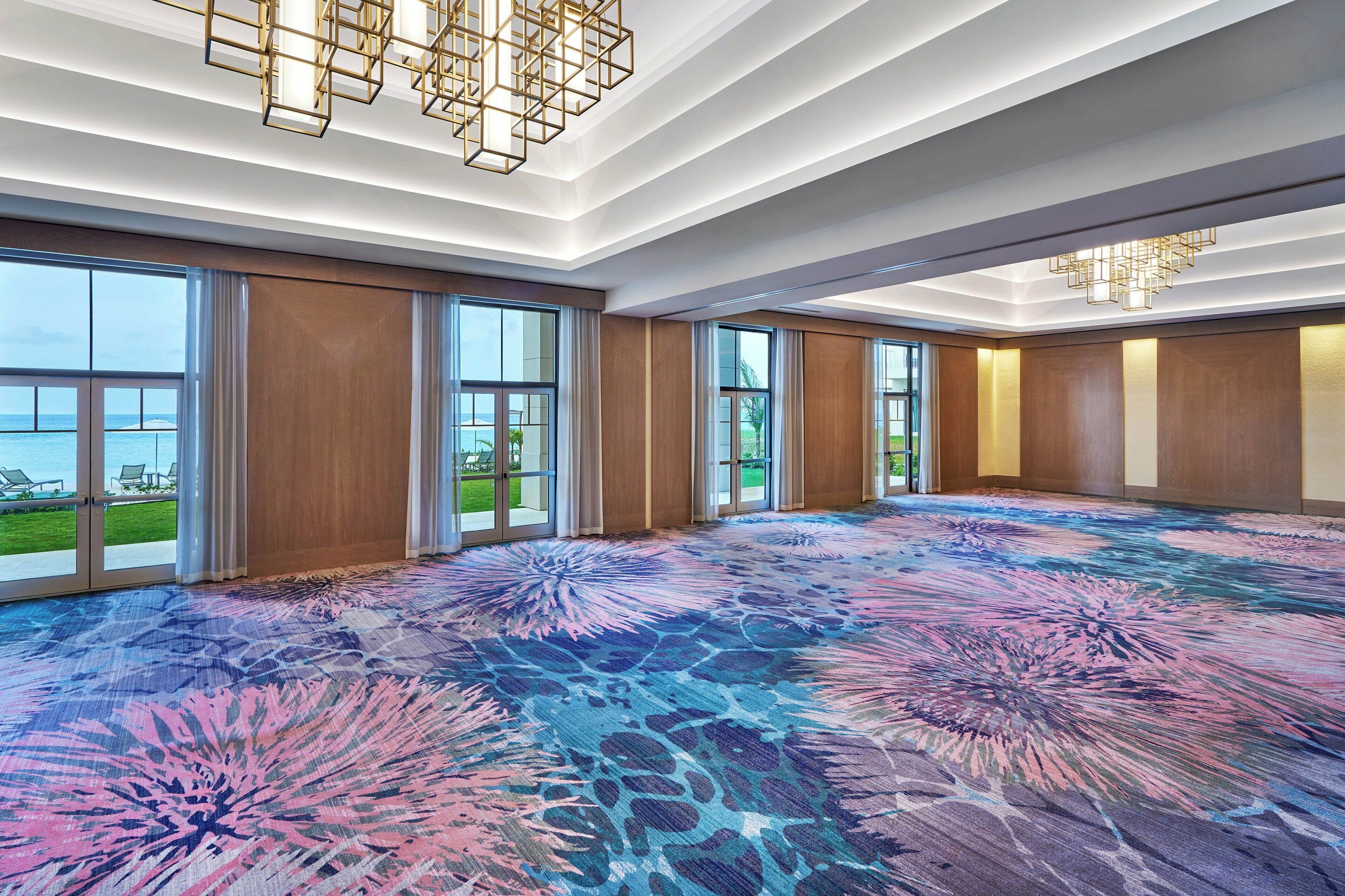A spacious room with large windows, a patterned carpet, and modern lighting fixtures.