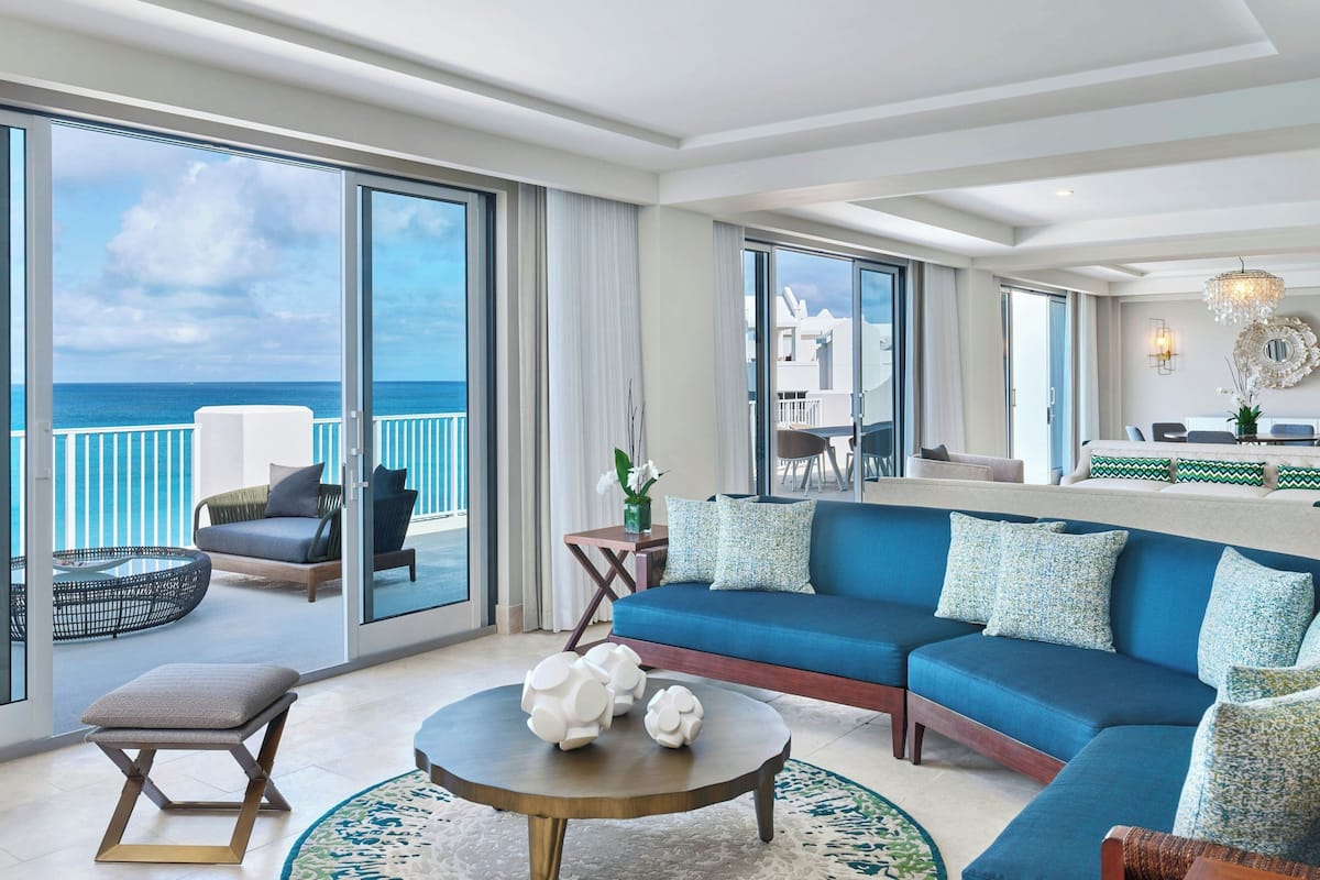 A spacious living area with a large sofa, a coffee table, and a view of the ocean through large windows.