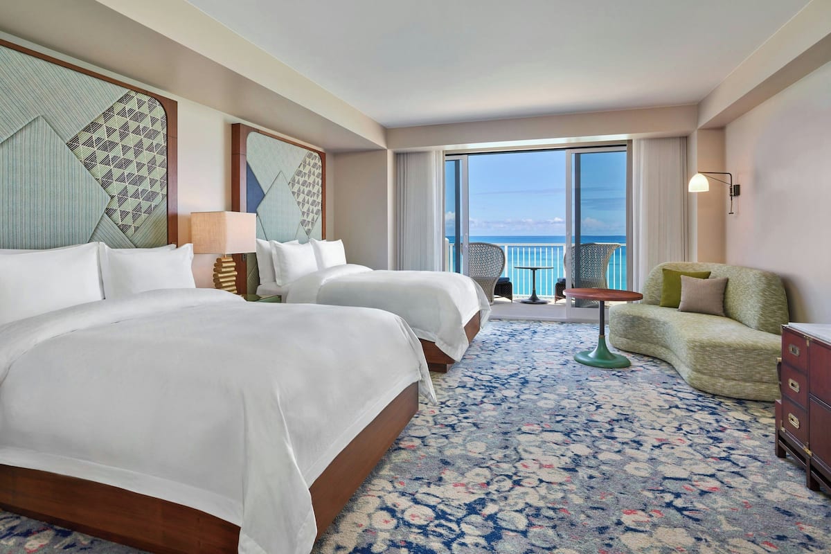 A hotel room with two beds, a balcony with a view, and a small seating area.