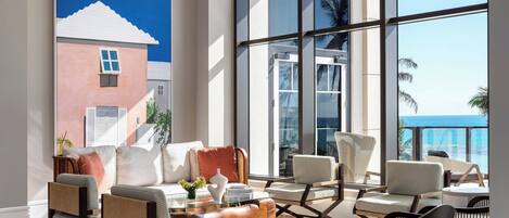 A spacious living room with a large window, a painting, and modern furniture.