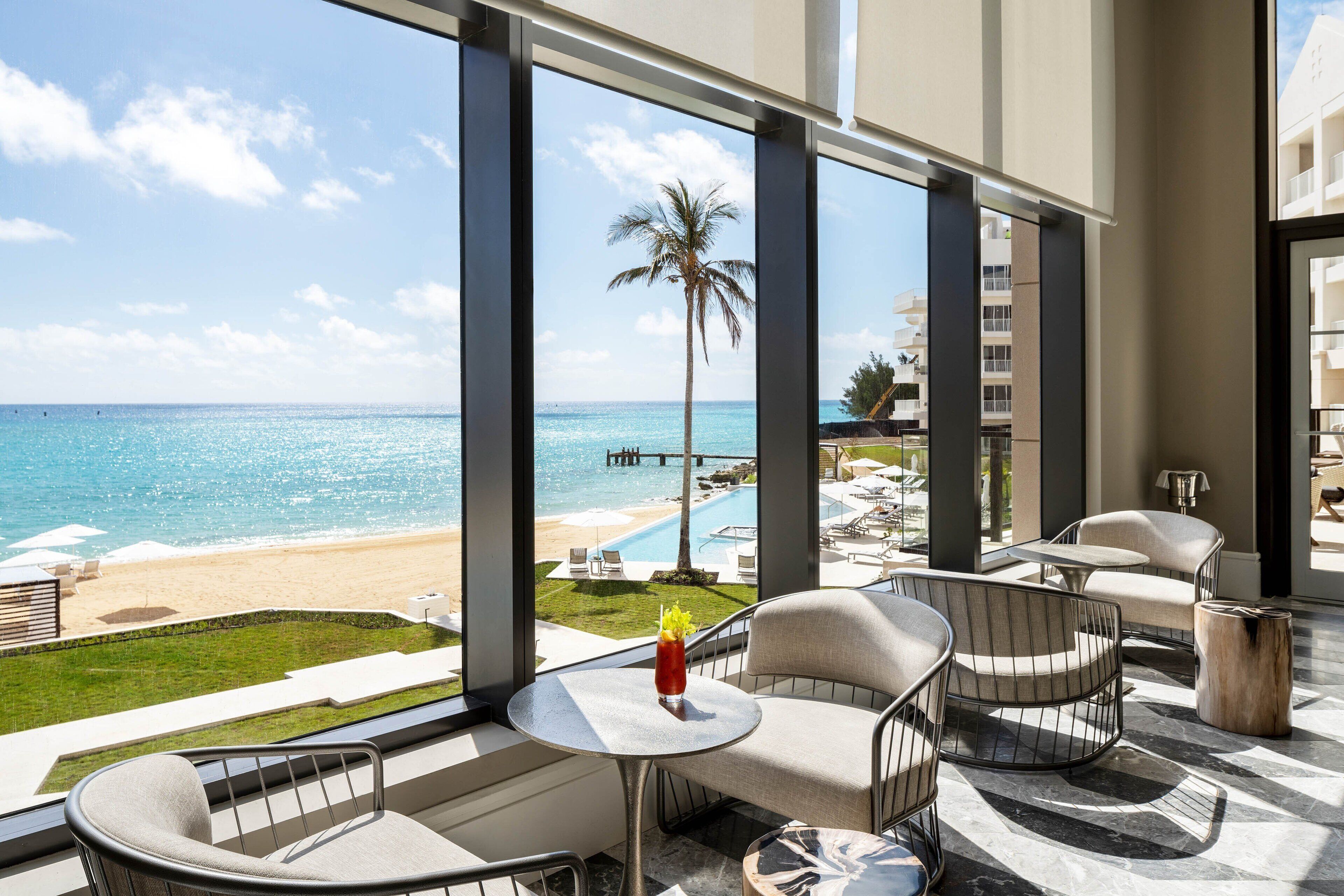 A balcony with a view of the beach and ocean, furnished with chairs and a table.
