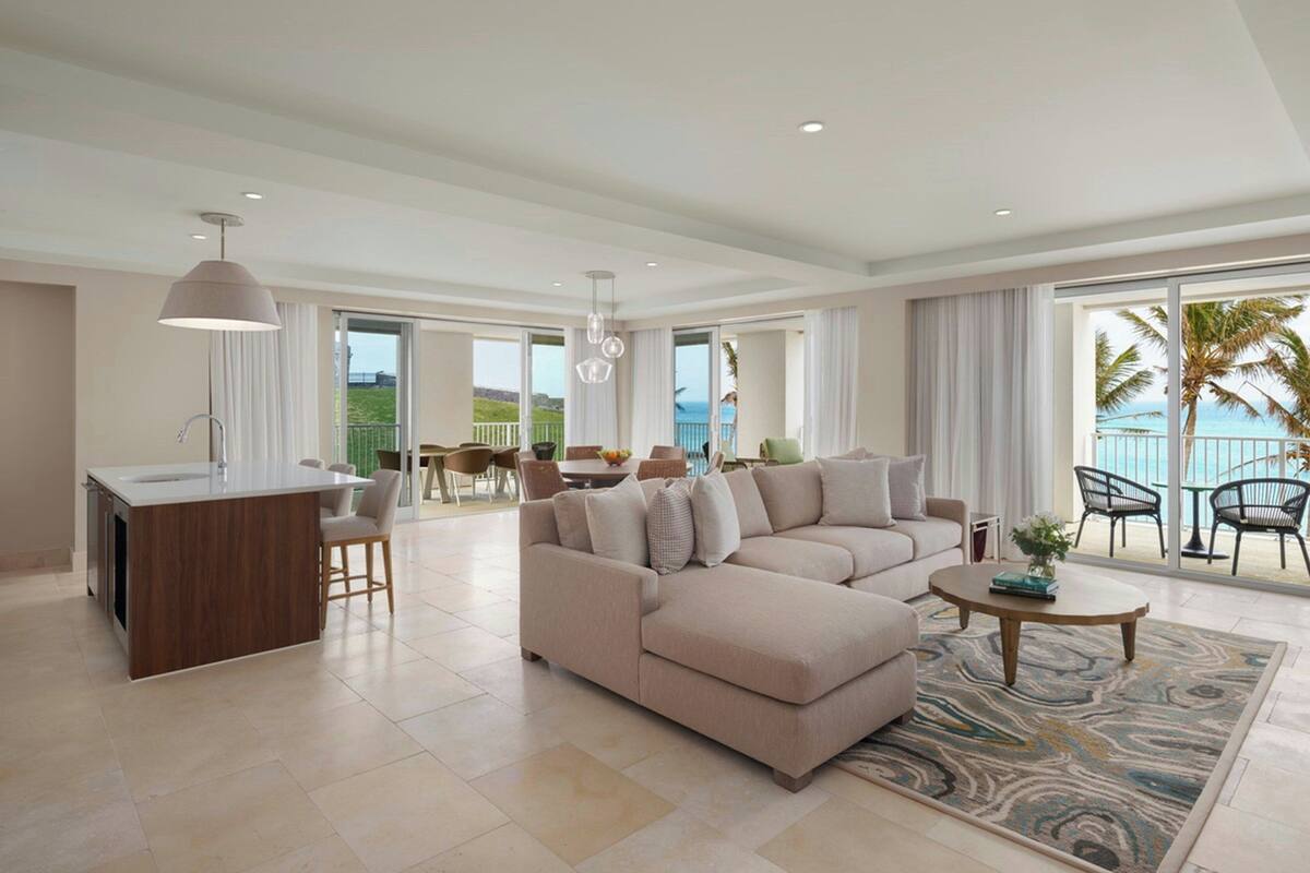 A spacious living area with a large beige sectional sofa, a round coffee table, and a kitchen island.