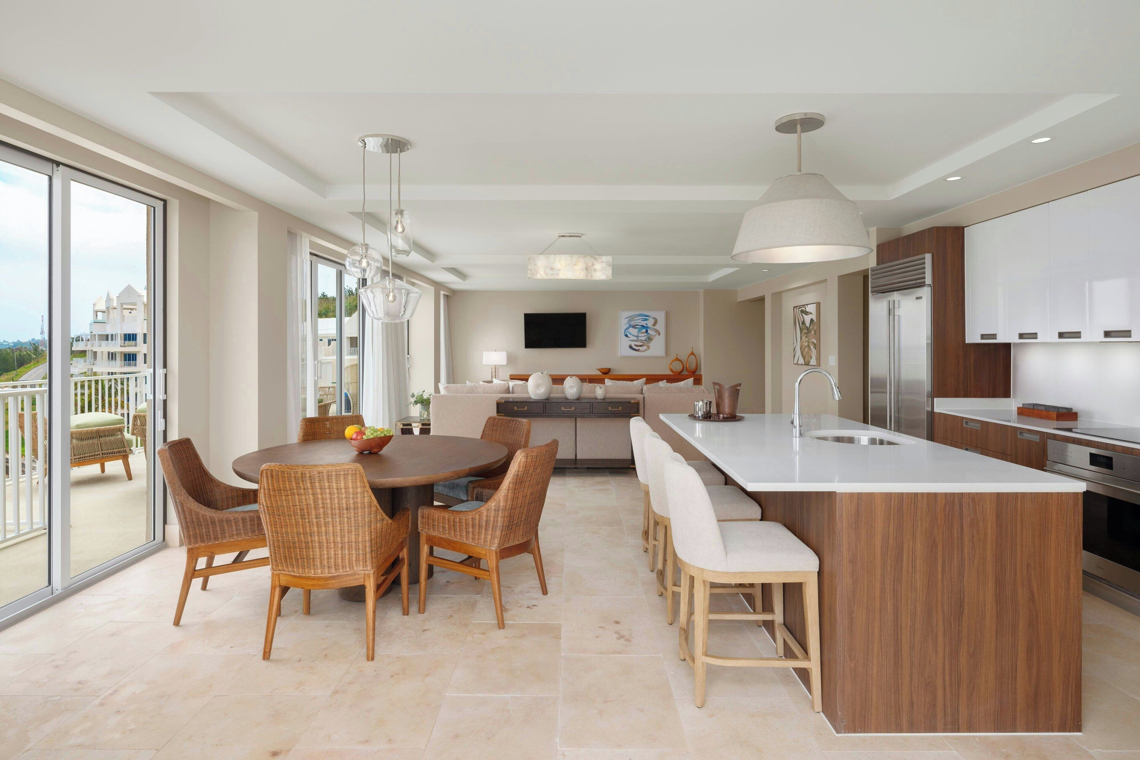 A modern kitchen with a central island, dining area with wicker chairs, and a large window overlooking a residential area.