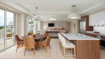 A modern kitchen with a central island, dining area with wicker chairs, and a large window overlooking a residential area.