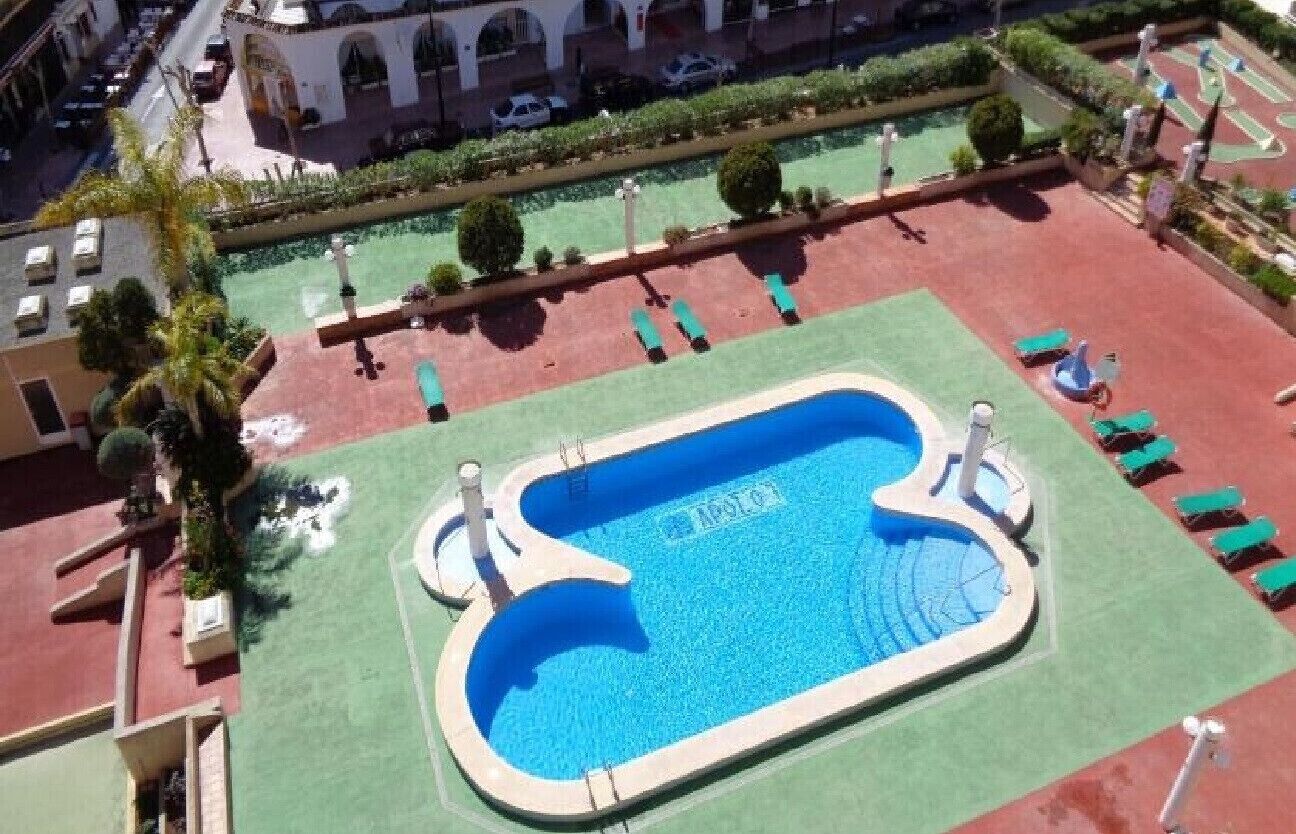 Vue aérienne d’un hôtel avec une piscine, une pelouse verdoyante et des chaises longues.