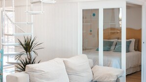 A modern living room with a white sofa, a staircase, and a bed in the background.