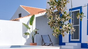 A white building with blue trim, a small outdoor seating area with a table and chairs, and a staircase leading to the entrance.