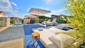Un área junto a la piscina con sillones de descanso, sombrillas y una pequeña mesa.