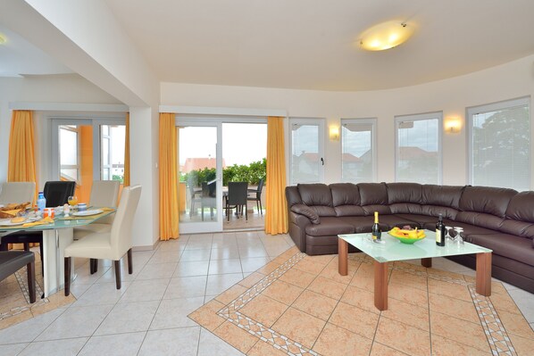 A modern living room with a glass dining table, a brown leather sofa, and a glass coffee table.