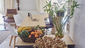 A dining area with a table set for two, featuring a fruit basket, dried flowers, and a bamboo plant. - Harmony Vale- Anavissos (Saronikos)