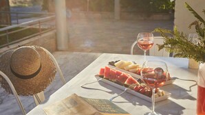 A table with a book, a hat, a plate of fruit, a glass of wine, and a potted plant. - Harmony Vale- Anavissos (Saronikos)