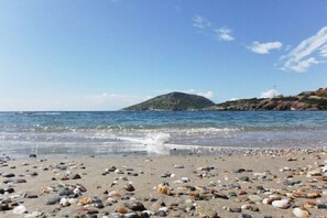 Una playa con piedras y una isla al fondo.