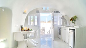 A bright, white interior with a kitchen and dining area, featuring modern furniture and a view through an open archway. - Fira-cave-sleeps 13-parking-pool-pet Friendly (Santorini)