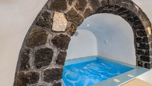 A stone archway leading to a blue-tiled pool area. - Fira-cave-sleeps 13-parking-pool-pet Friendly (Santorini)