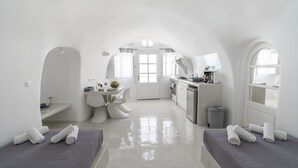 A compact, white-themed room with a kitchenette, a dining area, and two beds. - Fira-cave-sleeps 13-parking-pool-pet Friendly (Santorini)