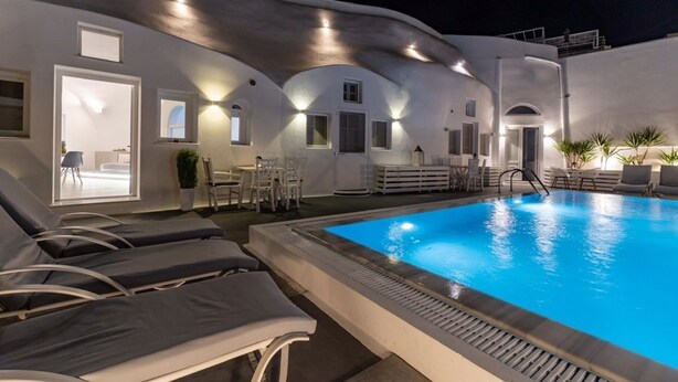 A poolside area with lounge chairs, a pool, and a dining area with tables and chairs. - Fira-cave-sleeps 13-parking-pool-pet Friendly (Santorini)