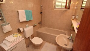 A bathroom with a bathtub, toilet, sink, and a towel rack with towels. - Apartment Kim (Lumbarda)