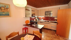 A compact kitchen with wooden cabinets, a dining table with chairs, and a painting on the wall. - Apartment Kim (Lumbarda)